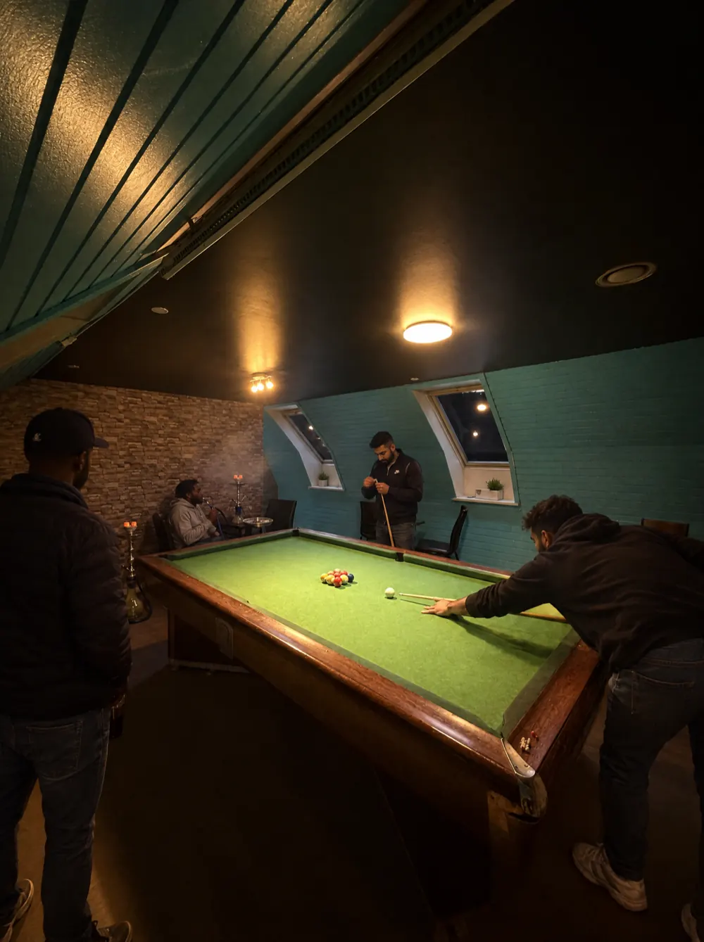 Et parti billard oppe under loftet med grønt klæde og blå trævægge